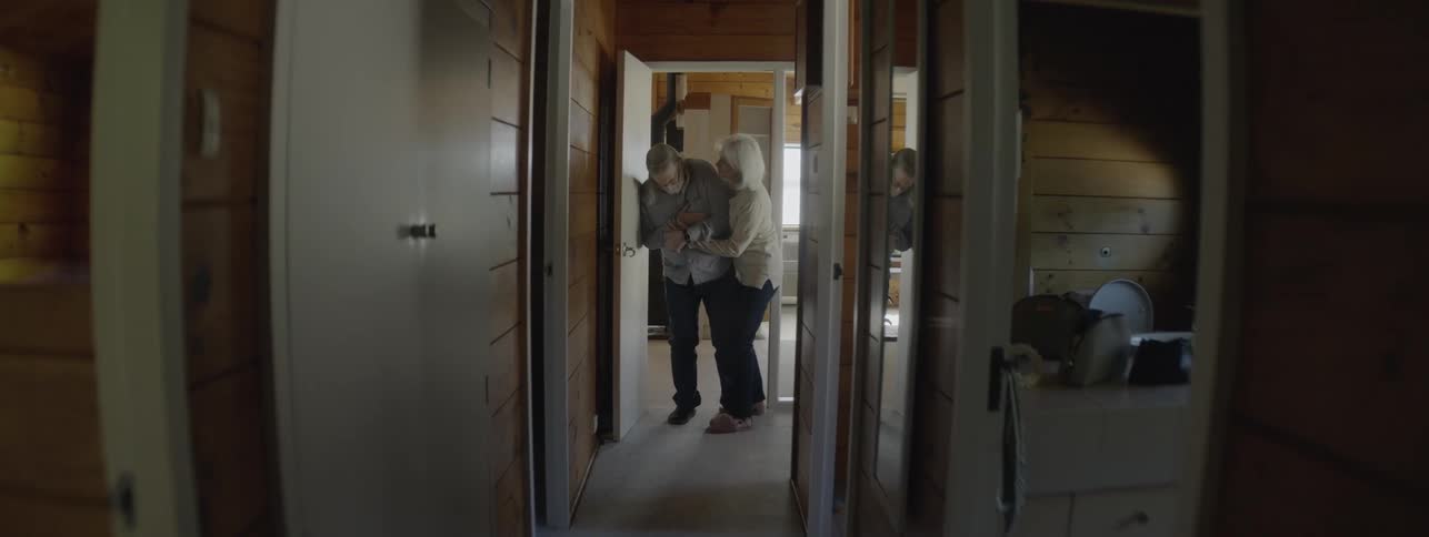 Elderly man feeling unwell being supported by a woman in a hallway at home