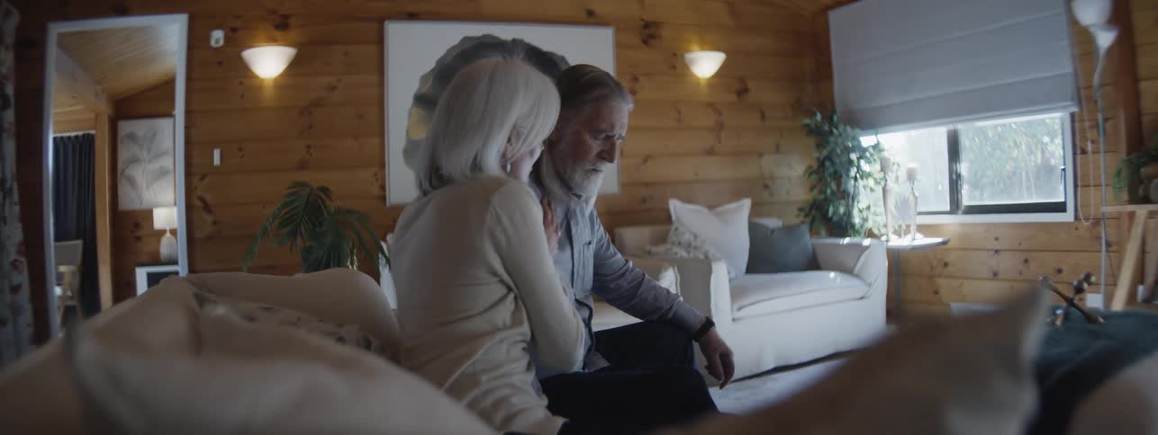A middle aged woman comforting her sick elderly partner sitting on a couch in the living room