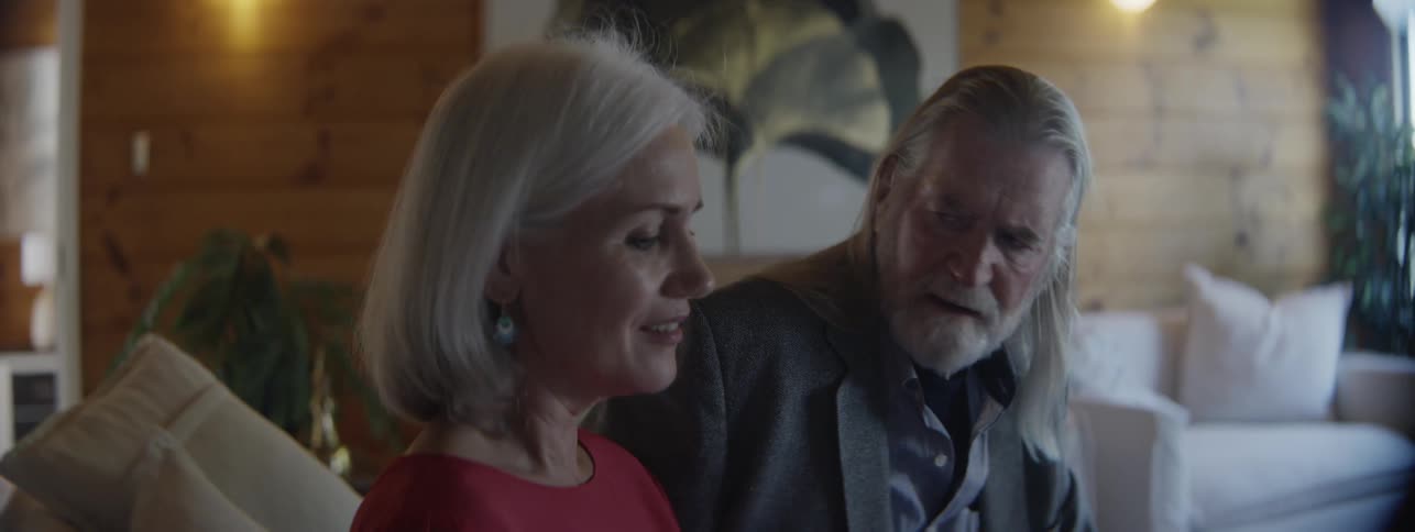 An older man and woman sit together on a couch while conversing