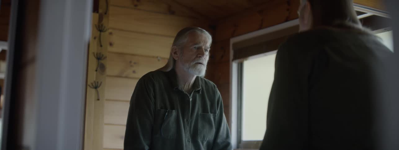 An older man thoughtfully in front of a mirror inside a wooden cabin