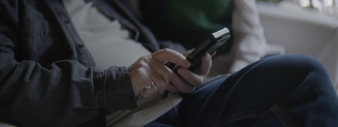 A person sits and holds a smartphone with both hands in an indoor setting