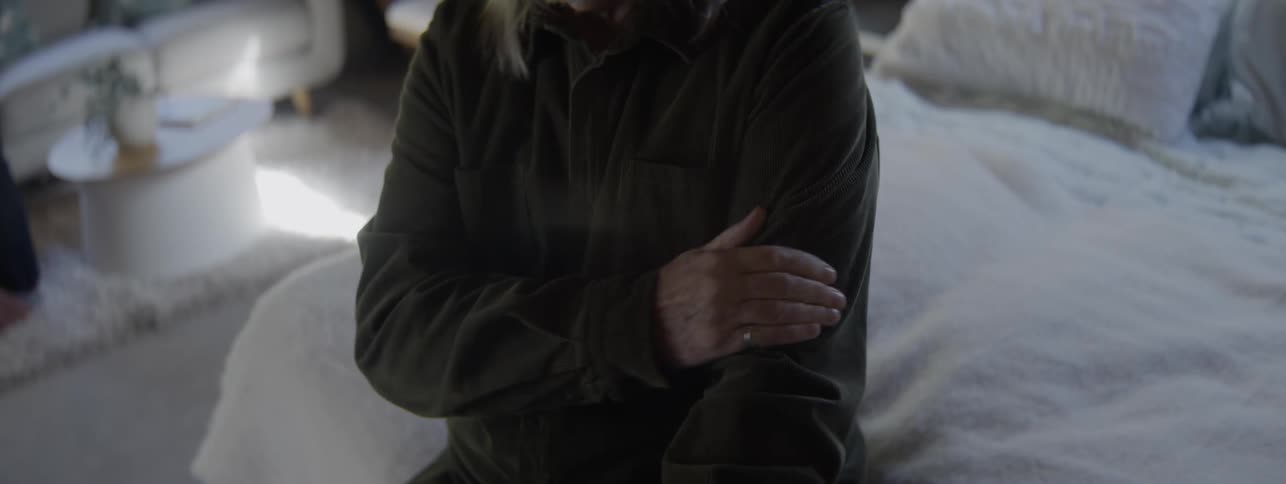Close up of an elderly man massaging his arm while sitting in bed in a bedroom during daytime