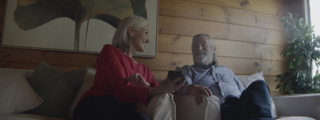 Woman showing something on her phone while talking and smiling with a man sitting next to her on the couch