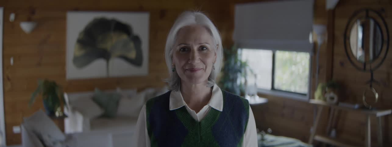 Grayhaired woman smiles in the center of a bright and cozy room