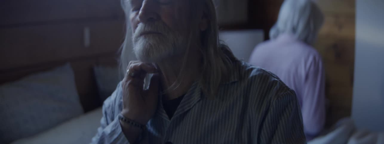 Close up of an elderly man bothered by body aches sitting in bed in a bedroom during daytime