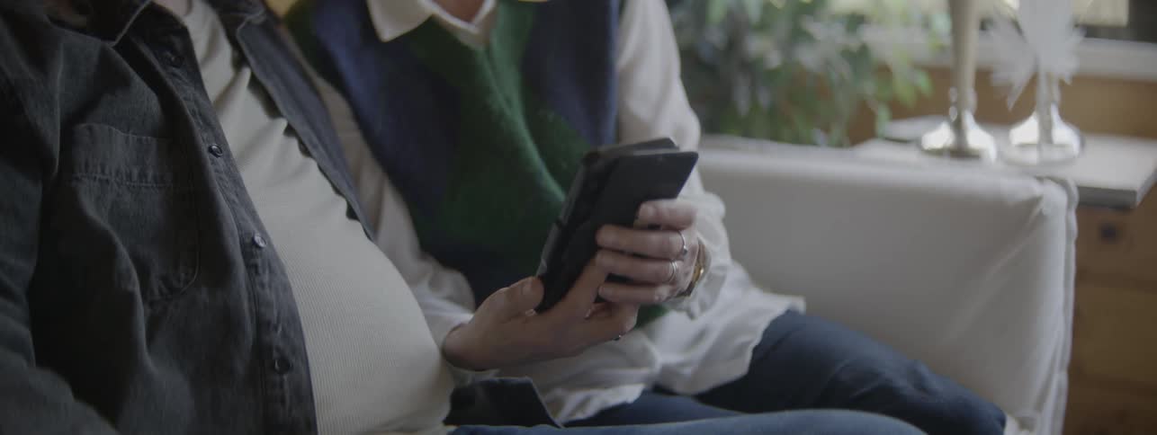 Elderly person using a smartphone beside another while sitting on a couch