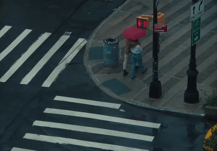 A couple walking across a wet asphalt crosswalk marked with white stripes sharing a bright red umbrella