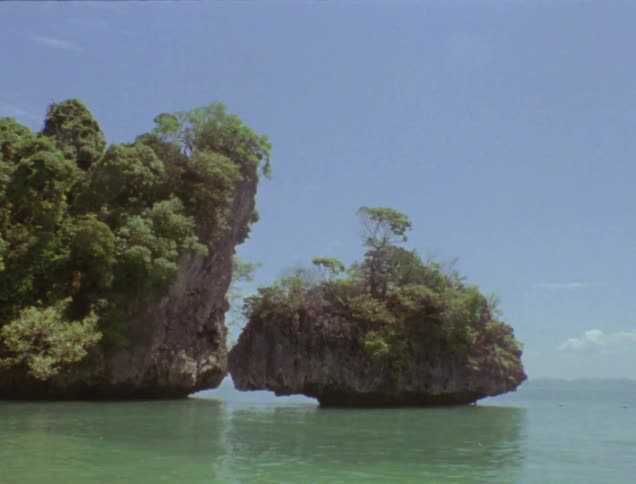 A rock formation covered with trees stands in the ocean