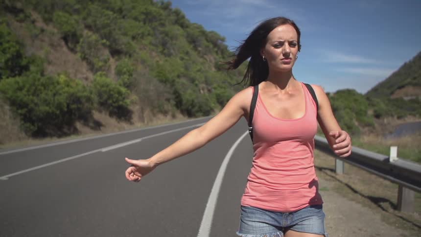 A woman hitchhikes on an empty rode