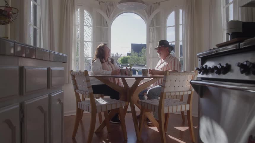 Couple sitting at a table having coffee and talking in a room lit by natural light