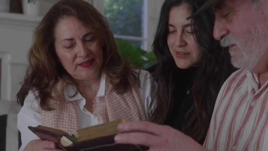 Close up of a family of three conversing while reading a book indoors during daytime