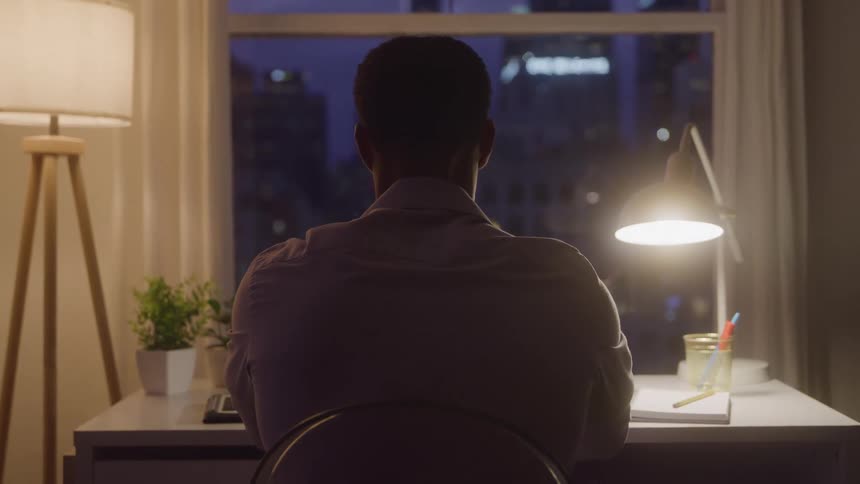 Person sitting at a lit desk at night with a city view through the window