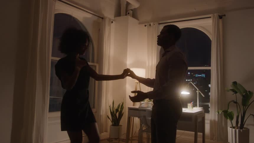 A man and woman dance together in an apartment at night