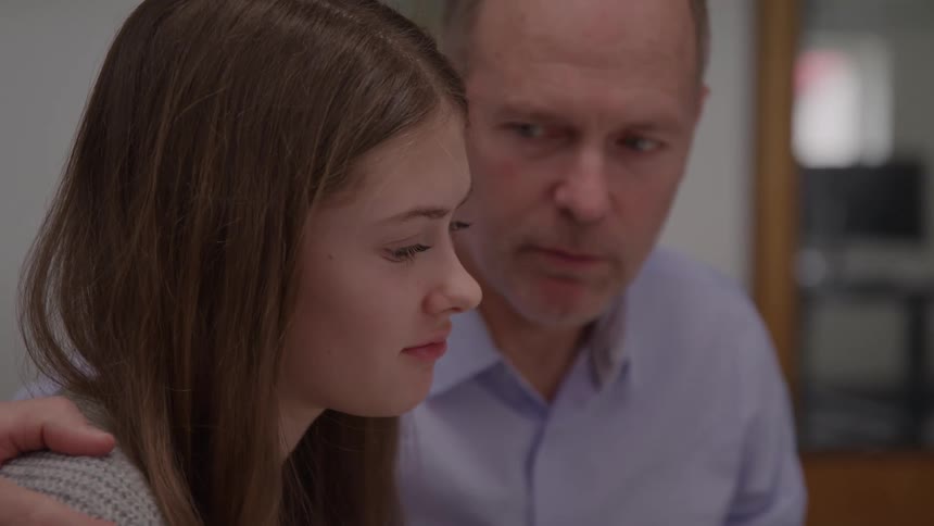 Father has his arm around his daughters shoulder and they look sad