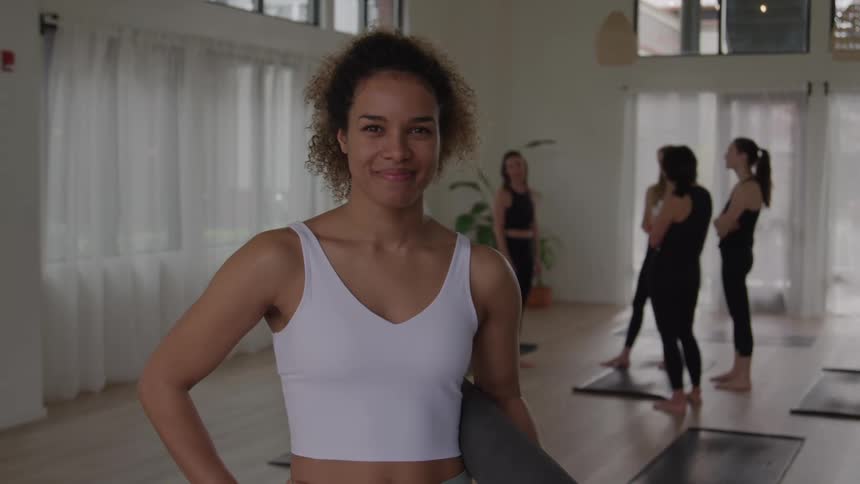 Woman smiles holding a yoga mat at the end of the class