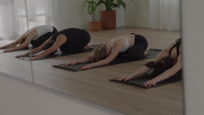 Practitioners perform childs pose aligned in a row during a yoga class