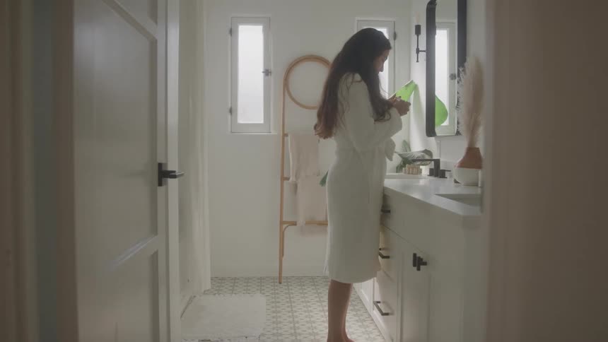 Woman in white robe stands up and picks up a pregnancy test from the sink in the bathroom