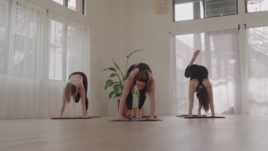 Three women perform a twisting pose in a yoga class