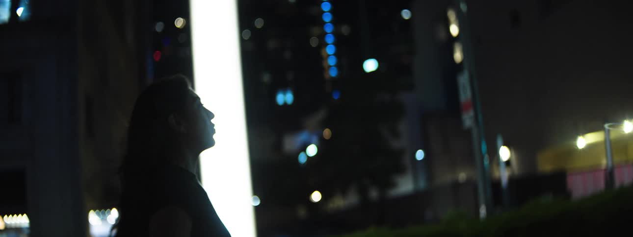 Woman walking outdoors at night with city lights in the background
