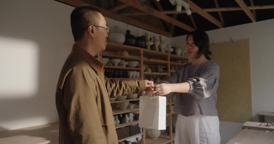 Man receives a bag from a woman in an indoor setting with shelves in the background