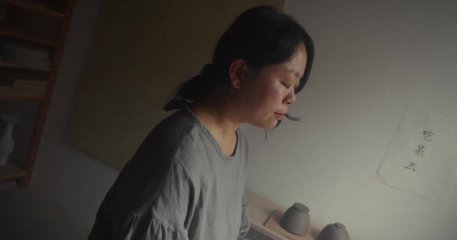 Woman sitting in a pottery studio looking out the window with a serene expression