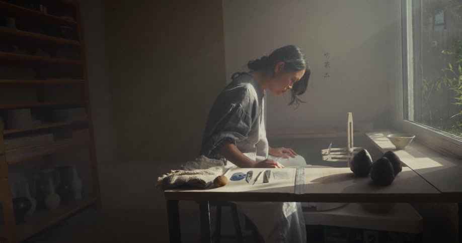 Potter shaping clay under soft light by a window
