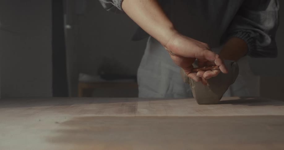 Hands cutting a block of clay on the worktable