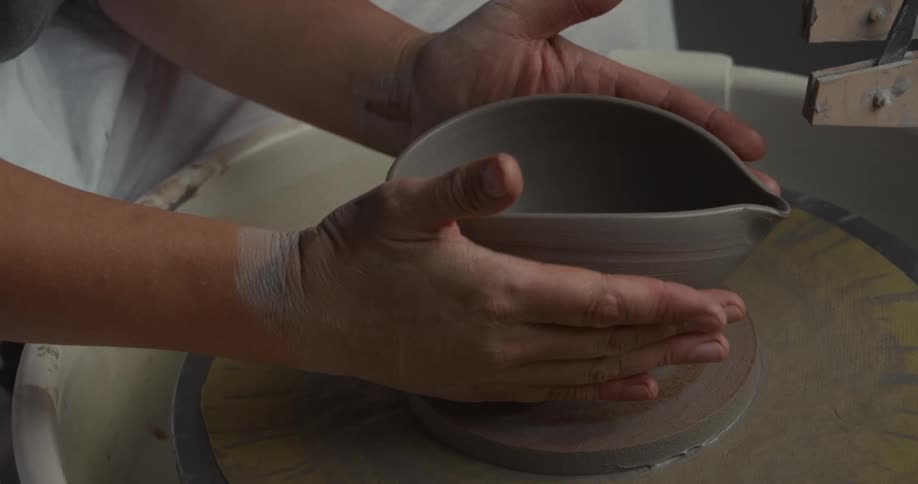 Hands shape a ceramic piece on a potters wheel