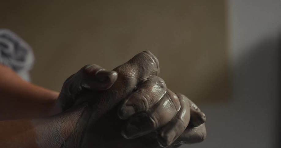 Hands covered in clay pressed together during the crafting process