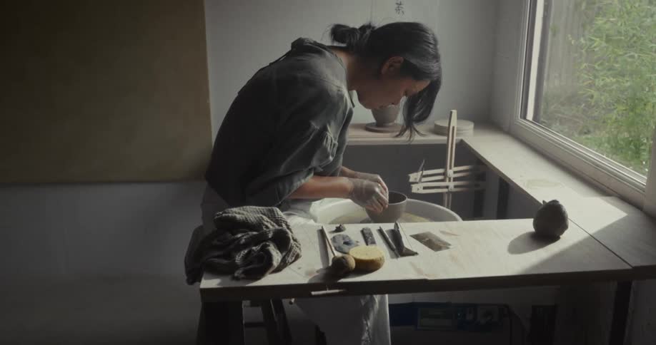 A young asian woman finishing clay pottery on a pottery wheel in a room during daytime
