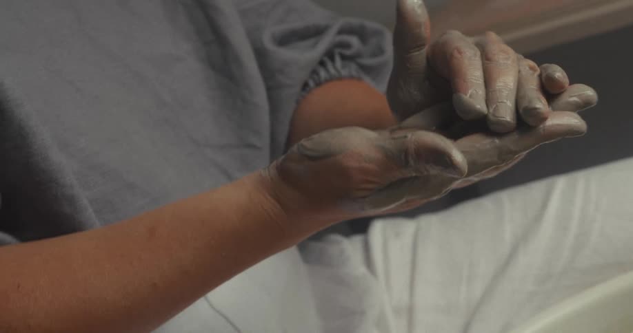 Hands covered in clay being shaped during the work