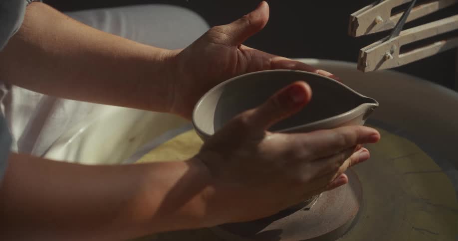 Hands holding a freshly shaped ceramic piece on the wheel