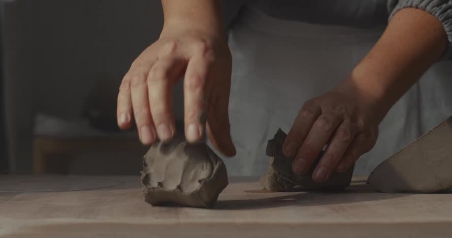 Hands manipulate pieces of clay on a work surface