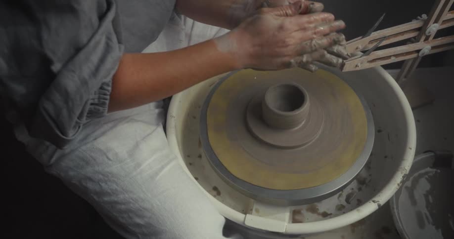 A person works at a rotating pottery wheel at midday shaping a vase from clay