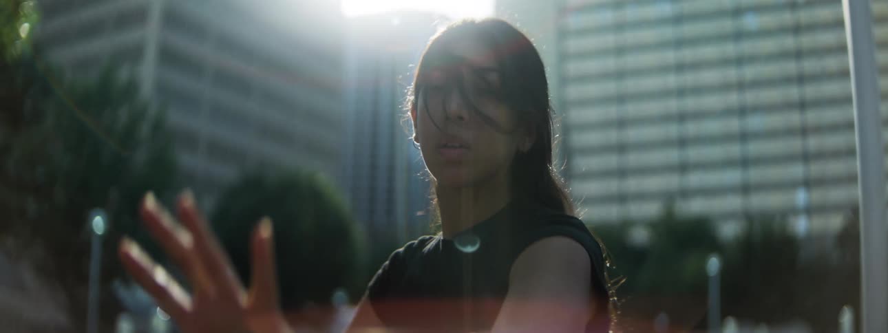 Woman dancing with expressive gestures under urban sunlight