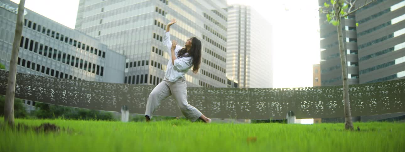 Woman dances barefoot on the grass in a city park located downtown on a summer day