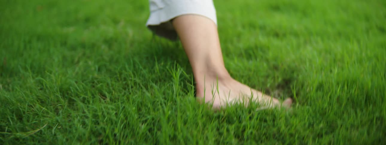 Two people from the knees down are barefoot and seem to be wrestling or playing around on grass