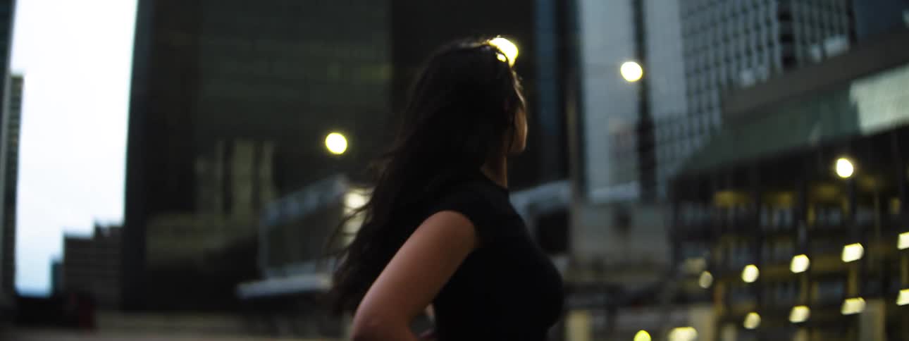 A woman with long dark hair dances outside in an urban setting