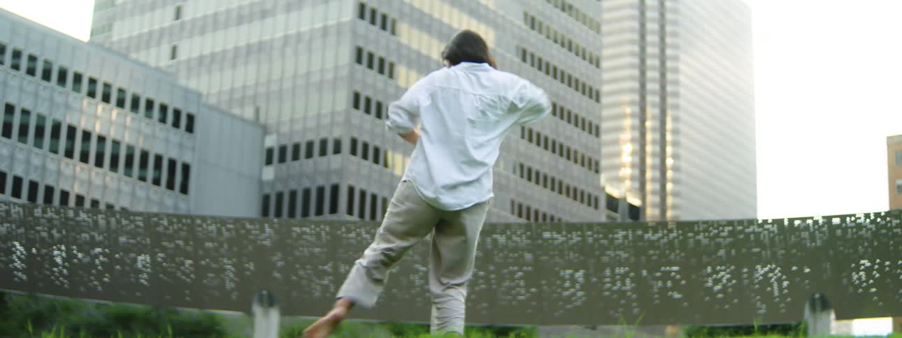 A female dances expressively on a bright green lawn near buildings