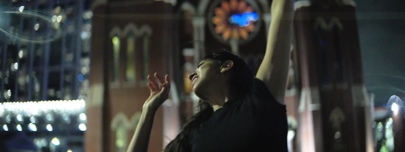 A female is dancing and smiling outside at night in front of a gothic style church