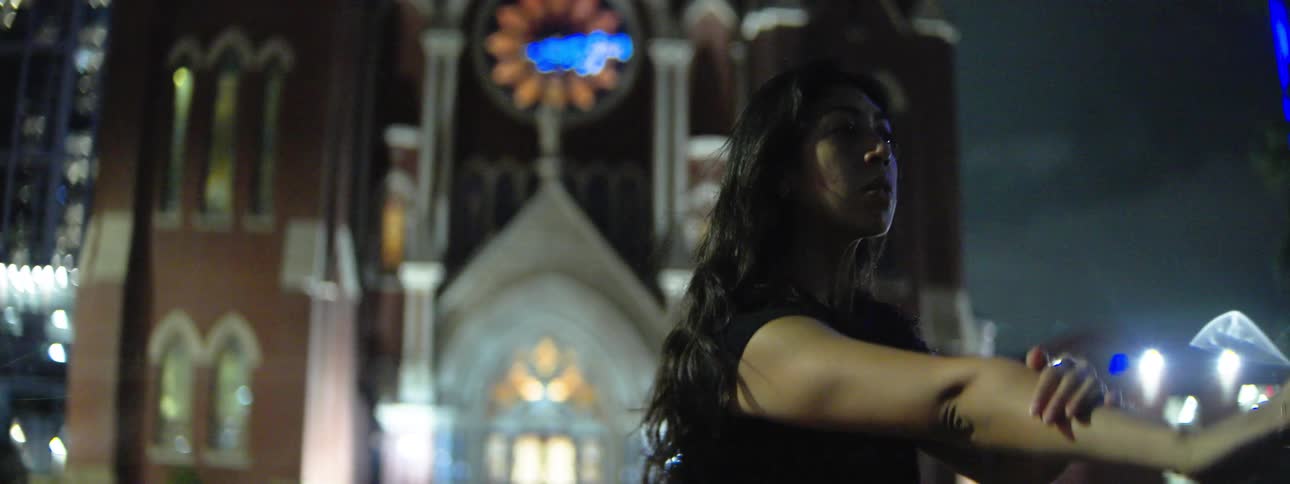 A woman dances outdoors at night in front of a cathedral