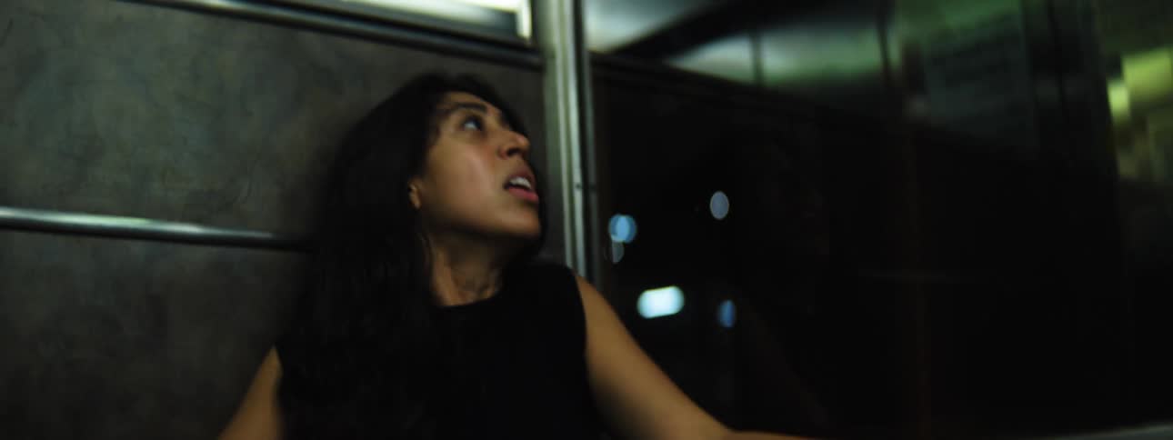 Female glances over her shoulder with anxious fear lips parted and eyes wideas she moves around in dim light