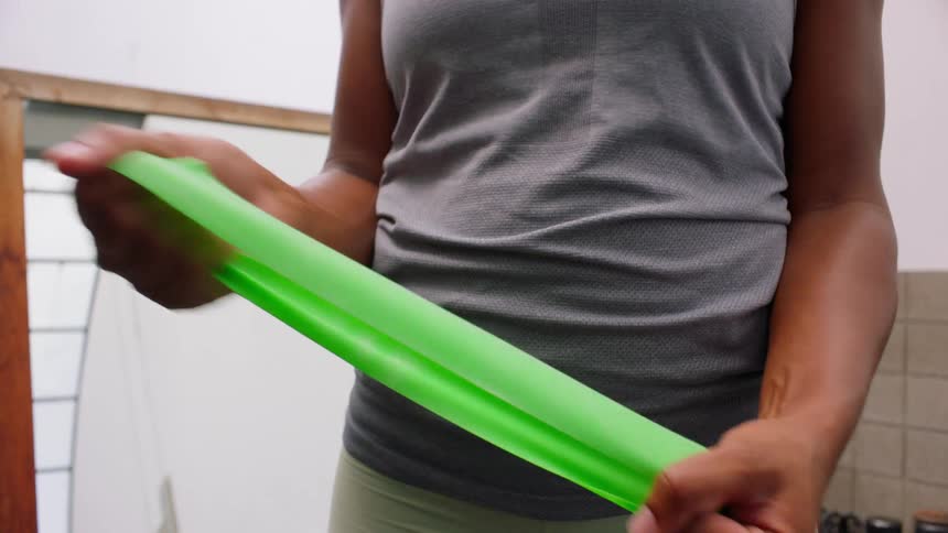 A black female from the arms down is stretching a neon green exercise band in a gym room