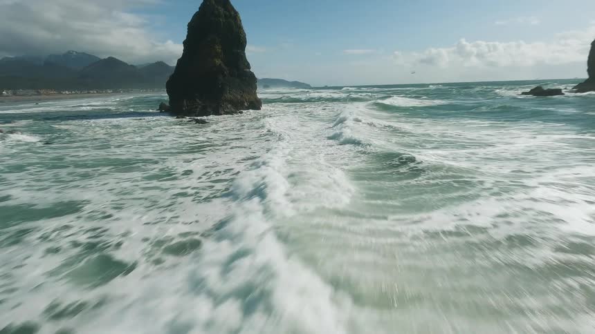 Aerial of ocean waves flowing and splashing against the coast during daytime