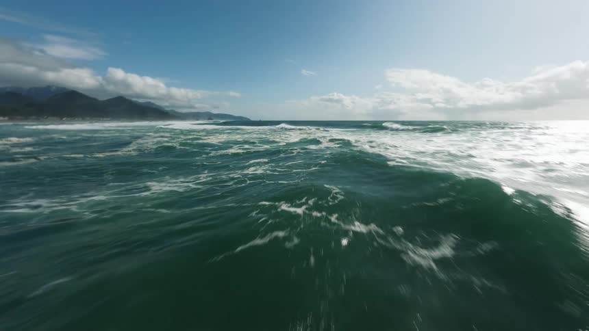 Choppy teal waves roll under a bright sky coastline and clouds tilting across the horizon