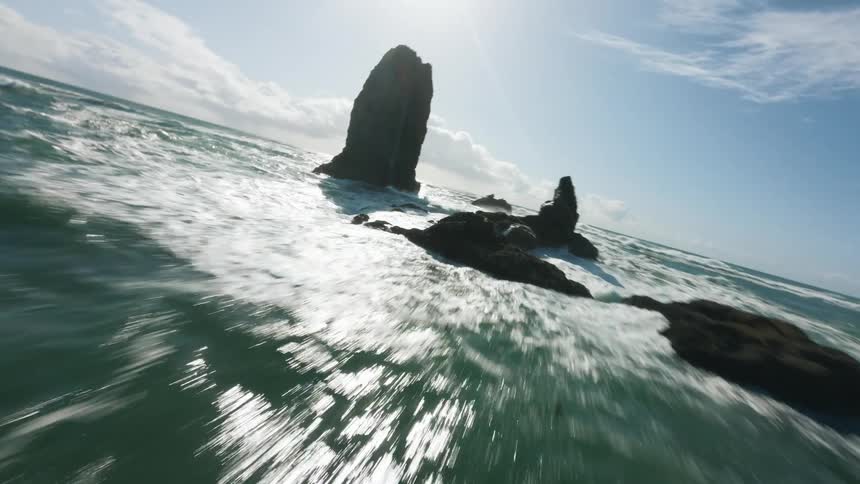 Aerial of sea waves flowing and splashing against rocks on the coast during daytime