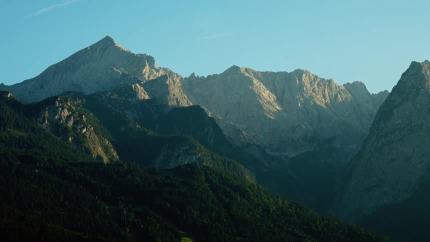 Rocky mountain range lit by sunlight with slopes covered by dense forests