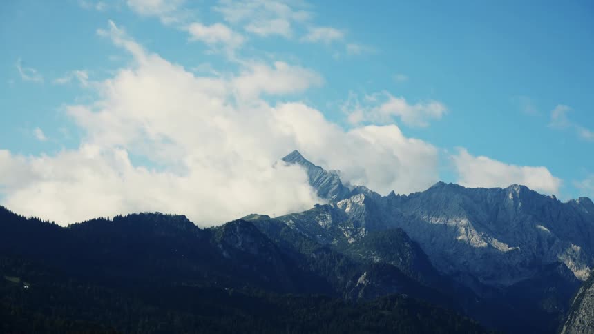 Sunlit mountain range stands out beneath a blue sky with white clouds