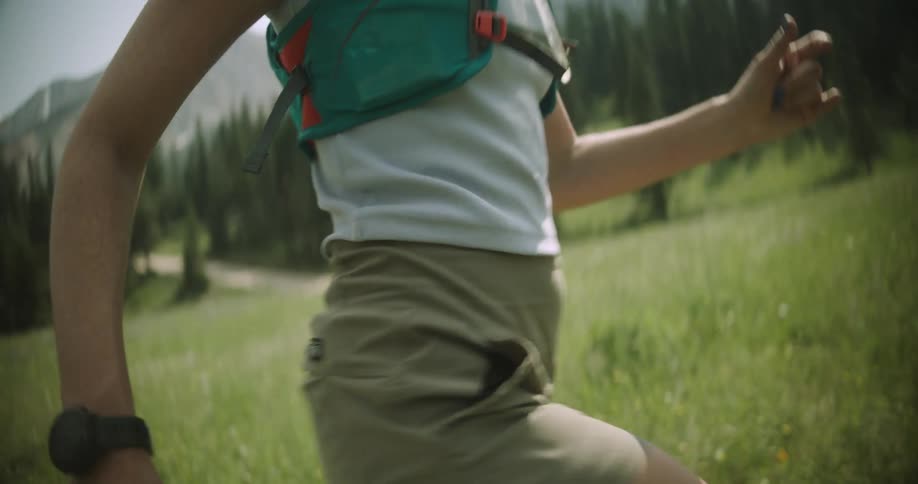 A woman running on a forest clearing wearing a vest with plastic tubes on it