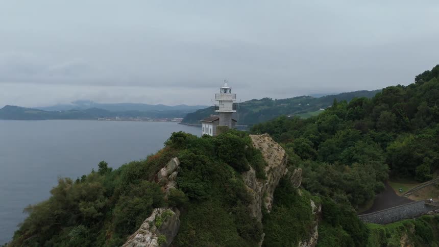 Lighthouse located on top of a cliff covered with vegetation by the sea